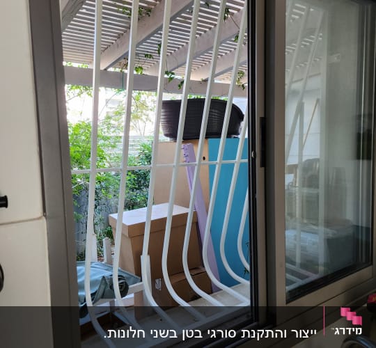 חלון עם סורגי מתכת לבנים ומסגרת אפורה
